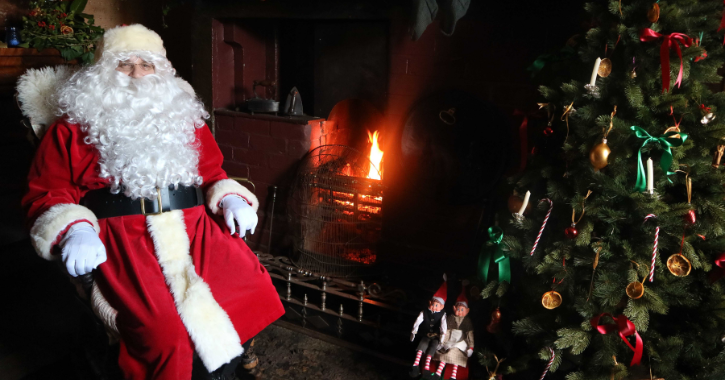 Father Christmas sat by roaring open fire and Christmas tree at Beamish Museum